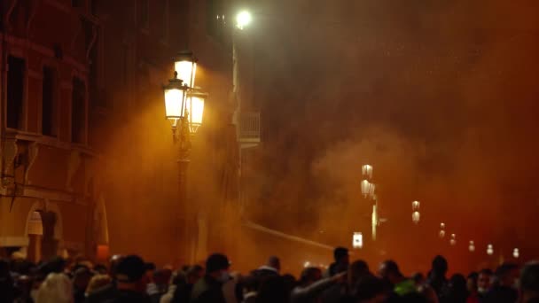 Натовп стоїть в помаранчевій димовій хмарі біля сяючих вуличних ліхтарів — стокове відео
