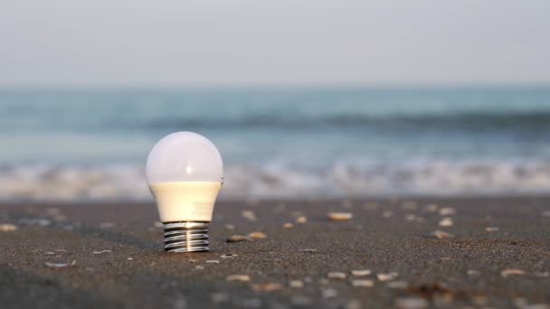 Stará LED žárovka uvízl v mokré moře pláž písek proti vlně — Stock video