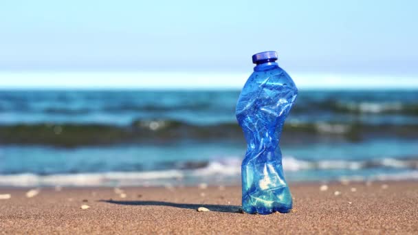 Crumpled blue plastic bottle stands on sand against sea — Stock Video