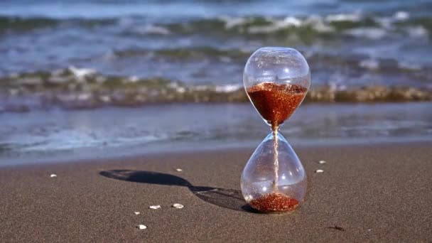 Reloj de cristal de arena con granos de oro se encuentra en la playa soleada — Vídeos de Stock