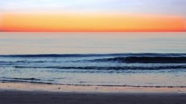 Deniz dalgaları, gün batımının güzel gökyüzüne karşı kumsalda yuvarlanır.