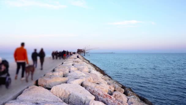 Люди гуляють по кам'яному причалу біля спокійного блакитного моря — стокове відео