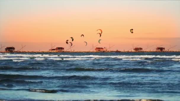 Ludzie kitesurfują nad błękitnymi falami o zachodzie słońca. — Wideo stockowe