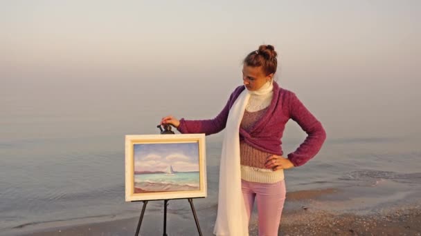 Elegante Frau steht neben Staffelei mit Meerlandmalerei — Stockvideo