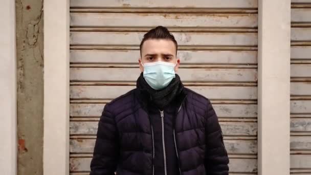 Mann mit medizinischer Maske steht neben hellgrauen geschlossenen Rollläden — Stockvideo