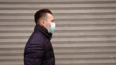 Tıbbi maskeli bir adam kapalı mağazalar boyunca yürür.