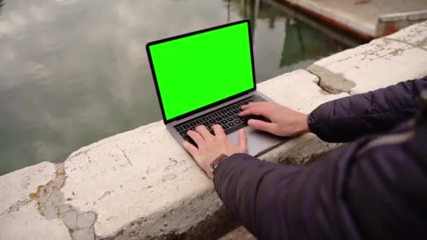 El hombre en la máscara trabaja en el portátil con la pantalla cromakey en el puente — Vídeo de stock