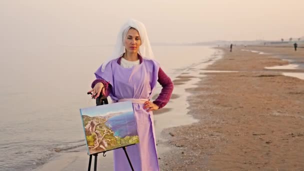 Гордая женщина позирует возле мольберта с удивительной морской картиной — стоковое видео