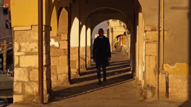 Uzun paltolu özgüvenli adam kanal boyunca yürüyor.