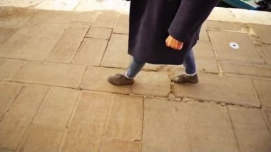 Zarif kot ve gri ayakkabılı adam cadde boyunca yürüyor.