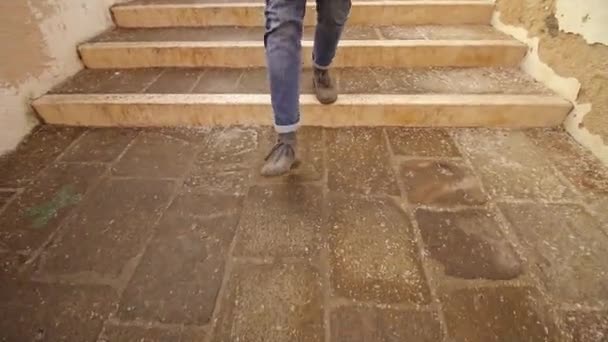Человек в синих джинсах и серой обуви спускается по каменной лестнице — стоковое видео