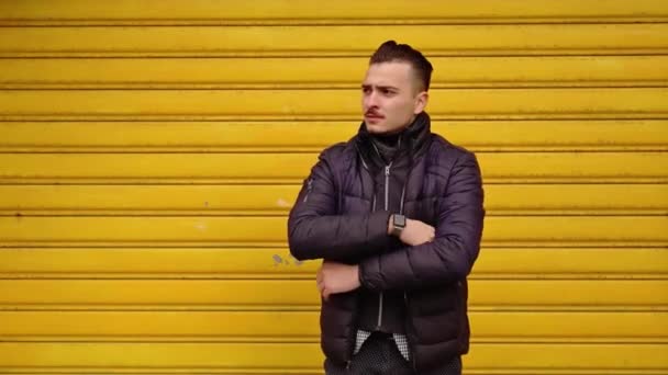 Junger Mann in warmer schwarzer Jacke wartet in der Nähe gelber Rollläden — Stockvideo