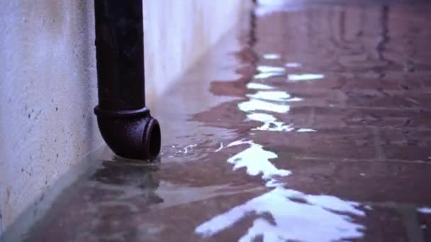 Flood water covers street by building with black drain pipe — Stock Video