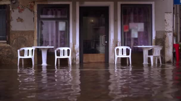 Plastikmöbel stehen neben Café-Fenstern in überfluteter Straße — Stockvideo