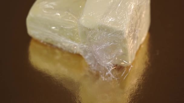 Verse boter omwikkeld met folie ligt op gouden spiegeloppervlak — Stockvideo