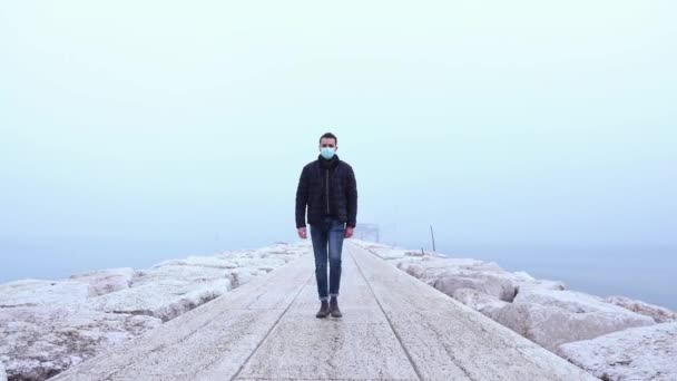Молодой высокий человек в защитной маске ходит по морскому пирсу — стоковое видео