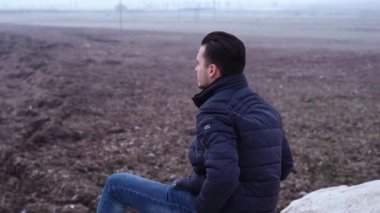 Dalgın adam engin gri denizde kumsal taşlarında oturuyor.