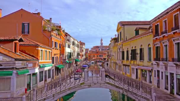 Мост через узкий канал с лодками среди красочных зданий — стоковое видео