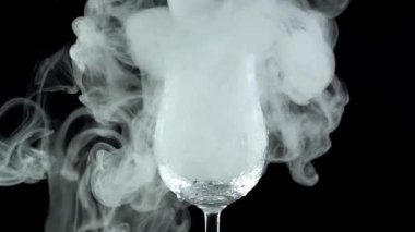 Siyah arka plandaki beyaz duman cam kadehe girer.