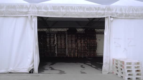 Movimento all'interno tenda bianca con pile di nuovi pallet di legno — Video Stock