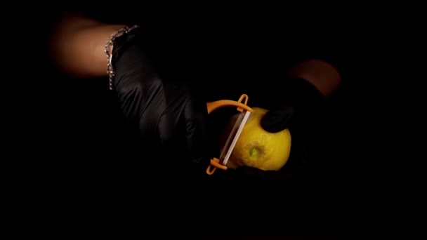 Person cuts zest from lemon with peeler on black background — Stock Video