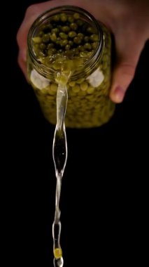 Adam kavanozdan siyaha terbiye edilmiş bezelye konservesi döker.