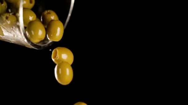 Verter sabrosas aceitunas verdes de vidrio sobre fondo negro — Vídeo de stock