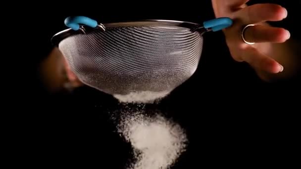 Woman sifts wheat flour shaking metal sieve on black — Stock Video