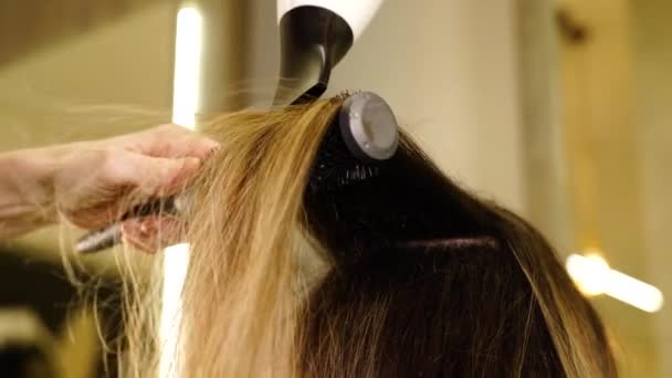 Дама вирівнює світле волосся клієнта пензлем і сушаркою — стокове відео