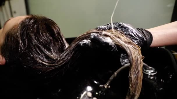 Парикмахер в перчатках выливает лосьон на длинные волосы леди в салоне — стоковое видео