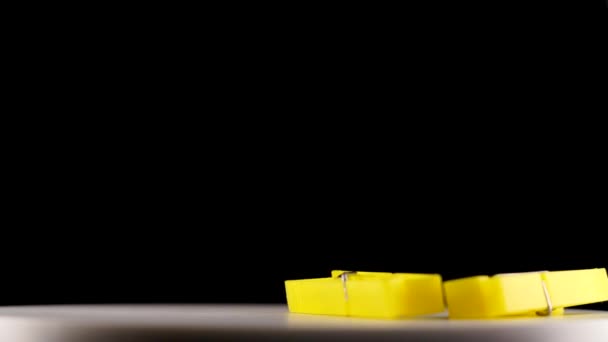 Yellow clothespins fall down onto table against darkness — Stock Video