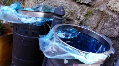 Mavi plastik torbalar ve oymalarla dolu gri metal çöp kutuları