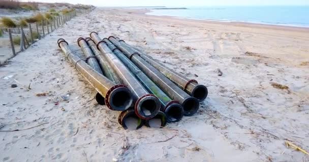 Tubos de metal negro se encuentran contra la valla en la playa con basura — Vídeo de stock