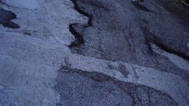 Küçük çukurları ve siyah çizgileri olan ıslak gri asfalt yolu
