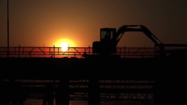 Köprüdeki kazıcının silueti ve geçen arabalar.