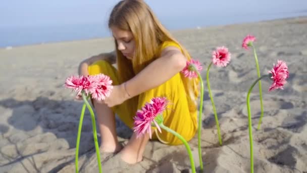 Дівчина сидить з квітами, посадженими на піску пляжу — стокове відео
