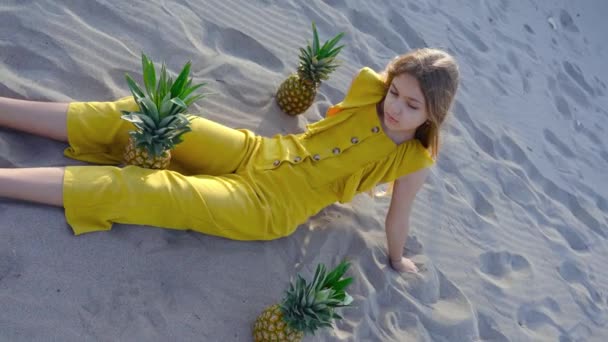 Giovane ragazza seduta sulla sabbia con ananas intorno — Video Stock