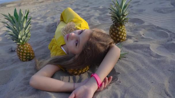 Giovane ragazza sdraiata sulla sabbia tra gli ananas — Video Stock