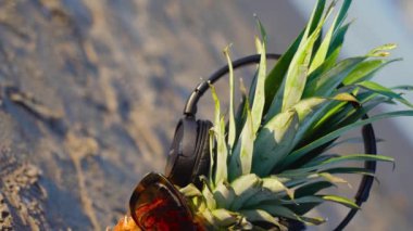 Deniz kumu üzerinde gözlüklü ve kulaklıklı ananas.