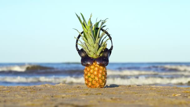 Piña con gafas y auriculares en la arena del mar — Vídeos de Stock