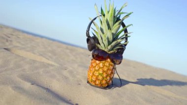 Deniz kumu üzerinde gözlüklü ve kulaklıklı ananas.