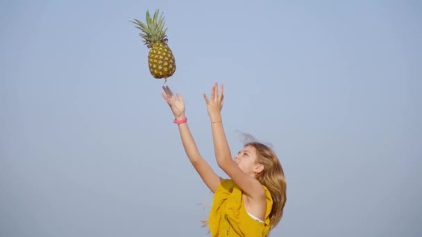Flicka kastar en ananas i luften i slow motion — Stockvideo
