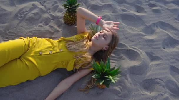 Jong meisje liggend op het zand tussen de ananas — Stockvideo