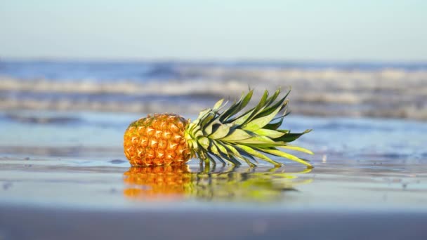 Ananász fekszik a homokon, a tenger hullámai mossák. — Stock videók