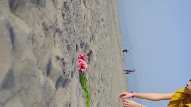 Teenager zvedne z písku kytici květin a hodí je na zem. — Stock video