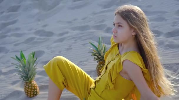 Giovane ragazza bionda seduta sulla sabbia tra gli ananas — Video Stock