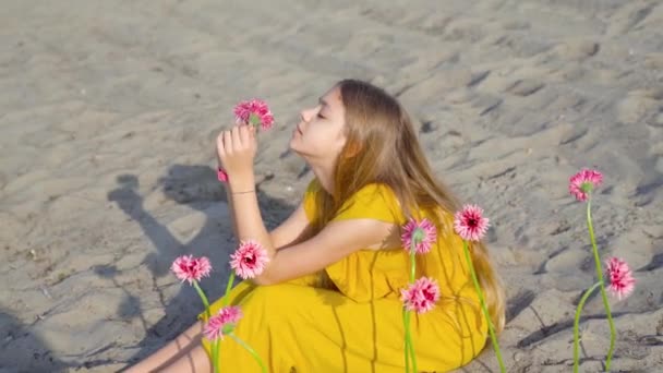 Chica vestida de amarillo sentada en la playa y rodeada de flores — Vídeos de Stock