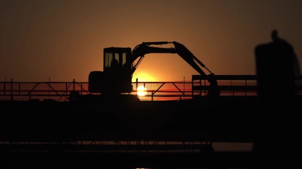 Silhouette of the excavator on the bridge with passing cars — Stock Video