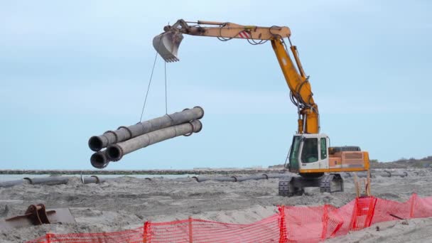 Excavatrice porte des tuyaux lourds sur la plage — Video