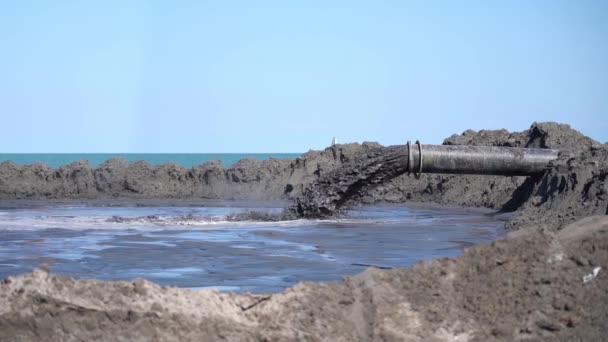 泥浆缓缓地从海滩上的管子里流出来 — 图库视频影像